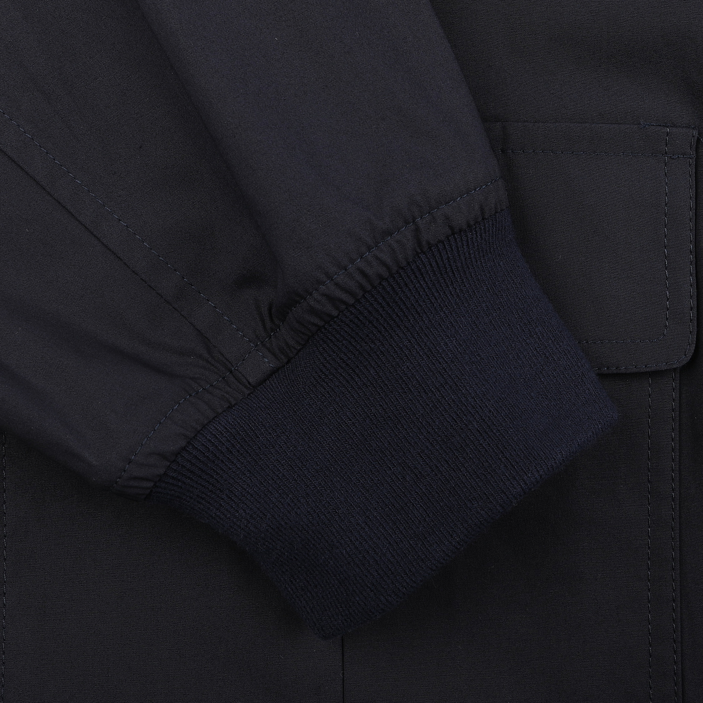 Close-up of a navy blue cotton sleeve with a ribbed cuff resting on matching fabric, reminiscent of an A-1 fighter pilot jacket. The Navy Blue Cotton Poplin Valstarino Jacket by Valstar features a visible pocket seam.