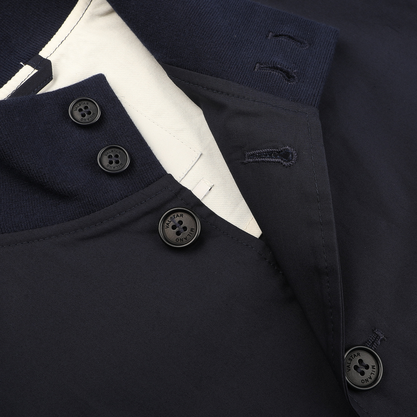 Close-up of the Navy Blue Cotton Poplin Valstarino Jacket collar by Valstar, featuring black buttons on a white lining. The collar, reminiscent of classic design, has buttonholes and a partially visible tag.