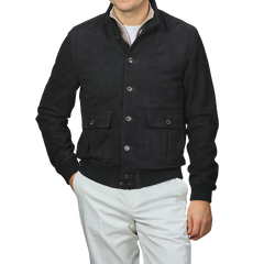 A man in a navy blue suede leather Valstarino jacket by Valstar and white pants stands against a plain background.