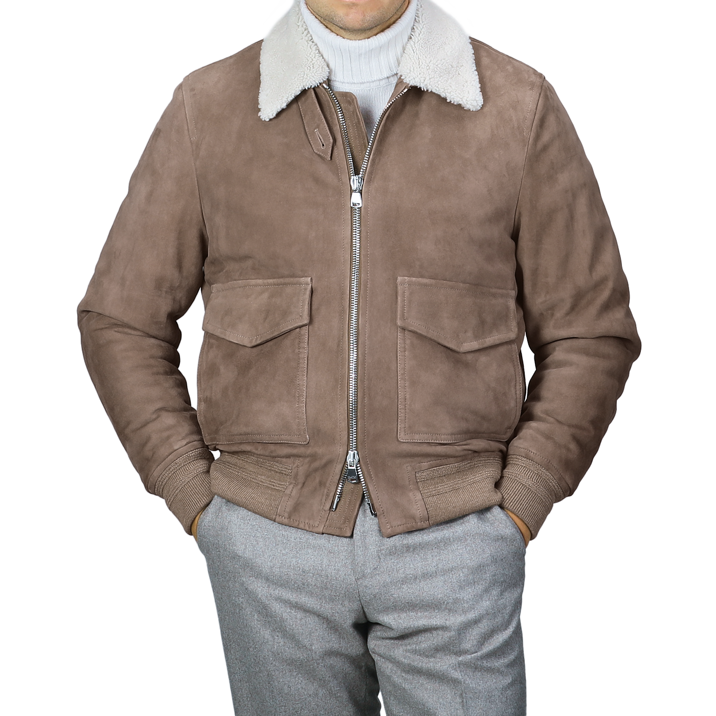 Wearing a Taupe Suede Leather Shearling Flight Jacket from Valstar over a white turtleneck, paired with gray pants.