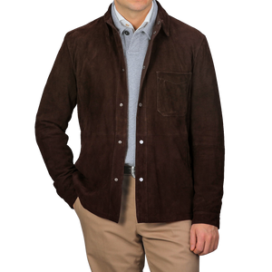 A person stands against a plain gray background, wearing the Dark Brown Suede Leather Amaro Shirt Jacket by Werner Christ over a light gray top and khaki pants, with one hand in their pocket.