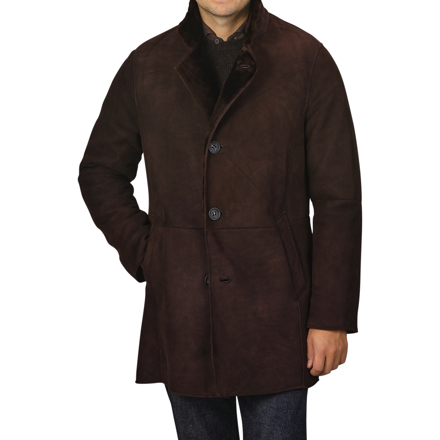 A person wearing a Werner Christ Dark Brown Suede Leather Blake Coat with three buttons is standing with one hand in their pocket against a plain background. The coat features a high collar and reaches mid-thigh, making it perfect for winter weather. The person's face is not visible.