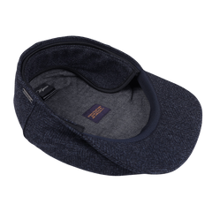 The Blue Herringbone Wool Ivy Contemporary Cap by Wigéns features a navy blue herringbone pattern crafted from pure wool. The interior, seen in the image, is lined with soft fabric and prominently displays a label.