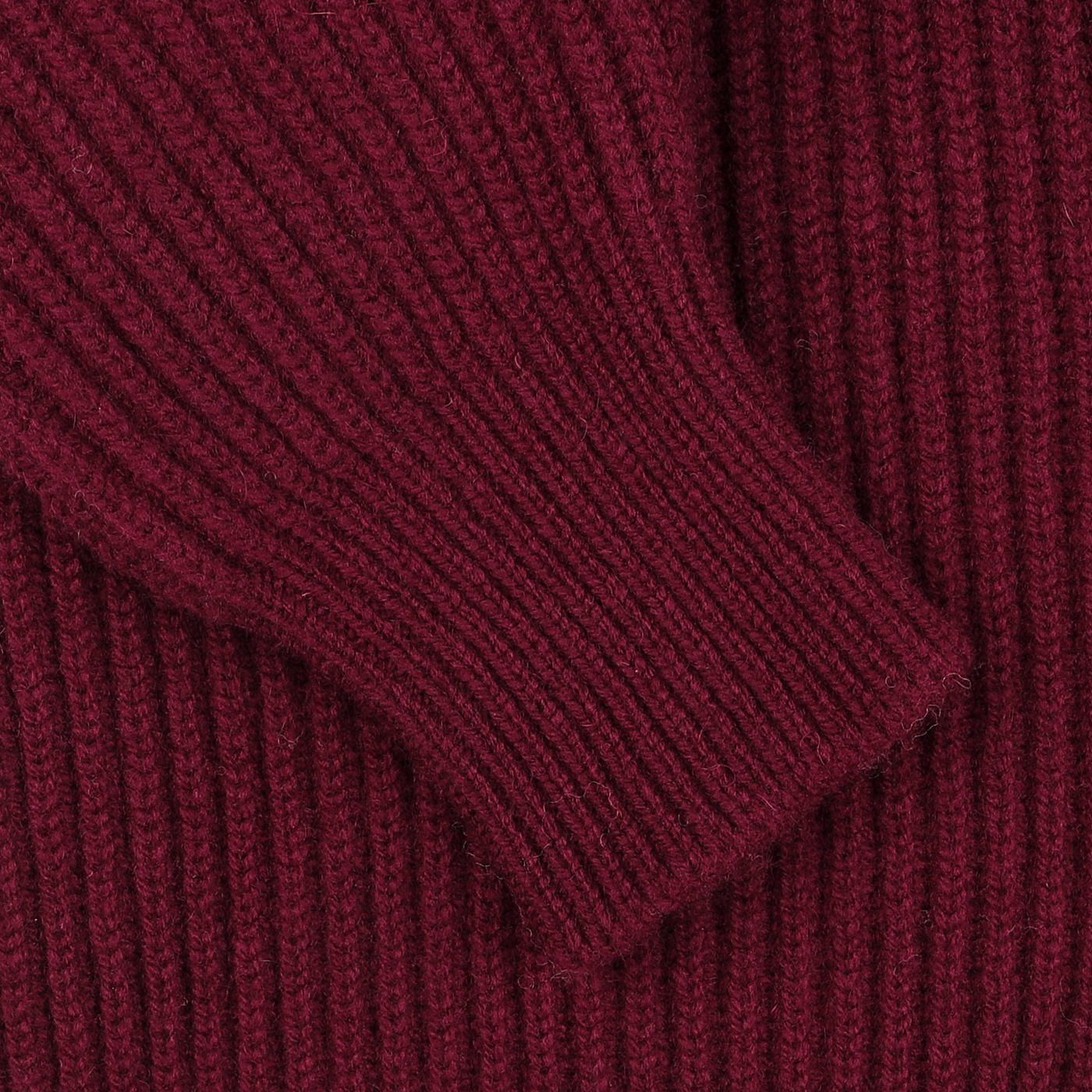 A close-up of a ribbed, maroon knit sleeve against a matching maroon fabric background, part of the luxurious Bordeaux Lambswool Shawl Collar Cardigan by William Lockie.