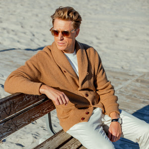 A man sitting on a bench wearing sunglasses and a William Lockie Brown Camel Hair Shawl Collar Cardigan.