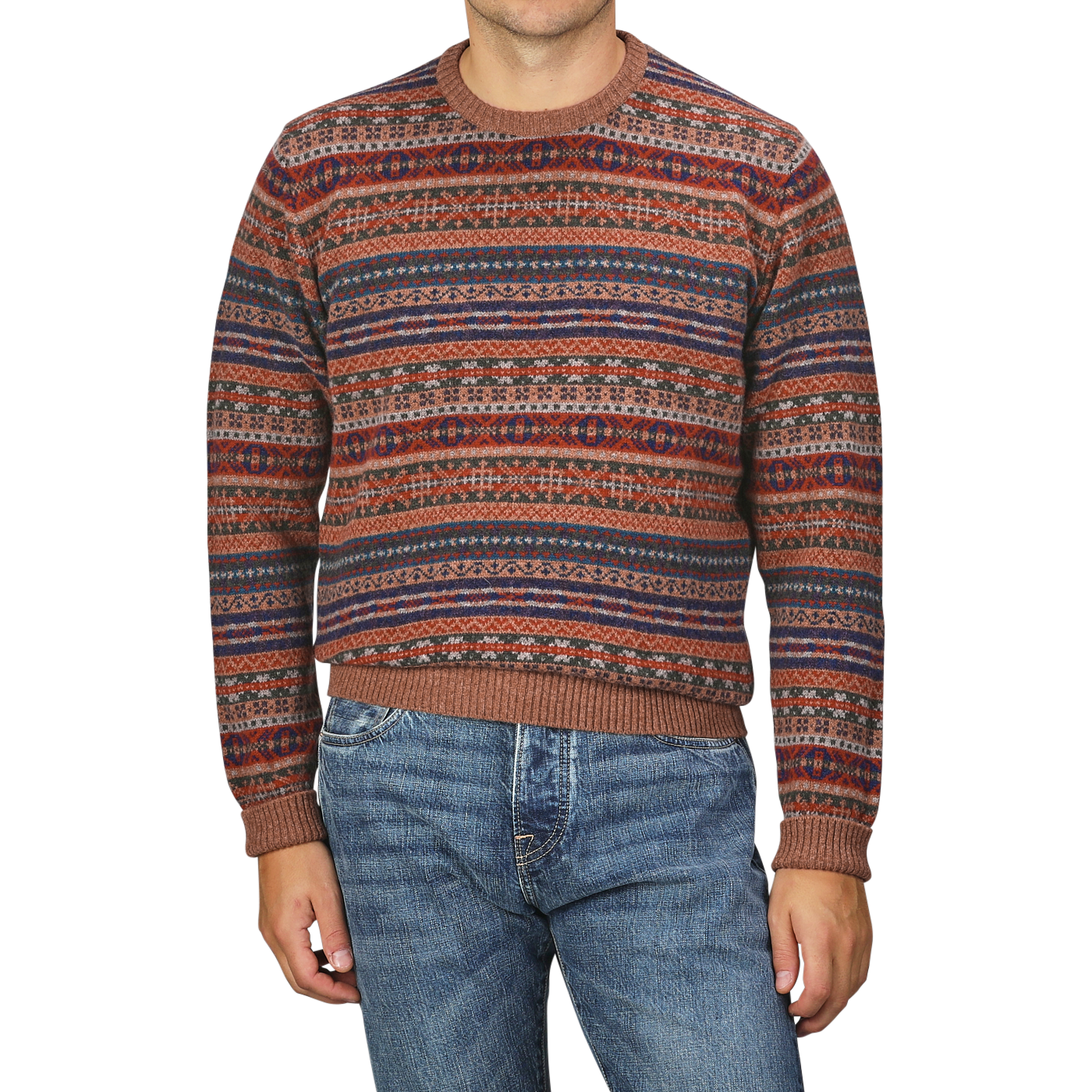 A person wearing a Brown Fair Isle Crew Neck Lambswool Sweater from William Lockie, featuring multicolored patterns, paired with blue jeans and standing against a plain background.