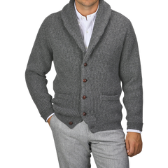 Person wearing a William Lockie Cliff grey lambswool shawl collar cardigan featuring brown buttons over a white dress shirt and grey pants. Only the torso and part of the arms are visible.