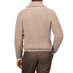 A person is seen from the back, dressed in a colt beige ribbed turtleneck sweater and soft brown pants. The attire exudes cozy elegance reminiscent of Scottish lambswool, distinctively styled without any leather buttons or a William Lockie Colt Beige Lambswool Shawl Collar Cardigan visible.