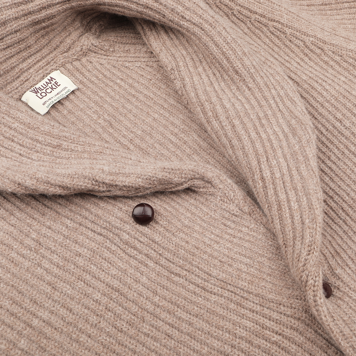 Close-up of the Colt Beige Lambswool Shawl Collar Cardigan by William Lockie, crafted from Scottish lambswool and featuring a label along with two striking leather buttons.