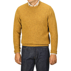 A person in a cumin yellow Cumin Brushed Shetland Lambswool Crew Neck sweater and dark jeans stands against a plain background, facing forward. This lambswool knitwear from William Lockie exudes timeless style and cozy warmth.