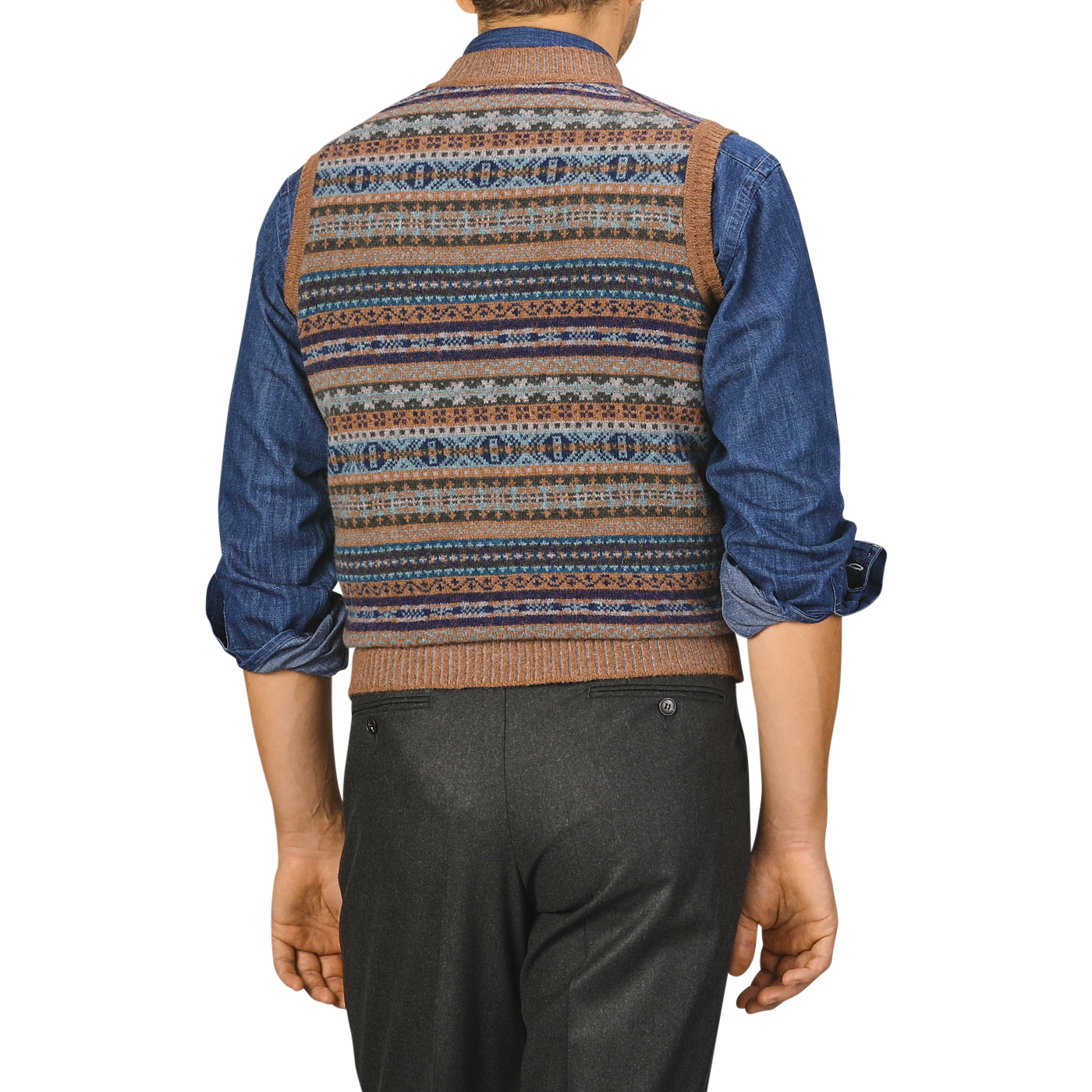 A person stands with their back to the camera, wearing a Driftwood Brown Fair Isle V-Neck Lambswool Slipover crafted by William Lockie over a denim shirt and dark trousers.