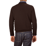 A person is standing with their back to the camera, wearing an Ebony Brown Crew-Neck Lambswool Sweater from William Lockie and blue jeans.