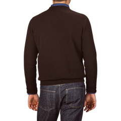 A person is standing with their back to the camera, wearing an Ebony Brown Crew-Neck Lambswool Sweater from William Lockie and blue jeans.