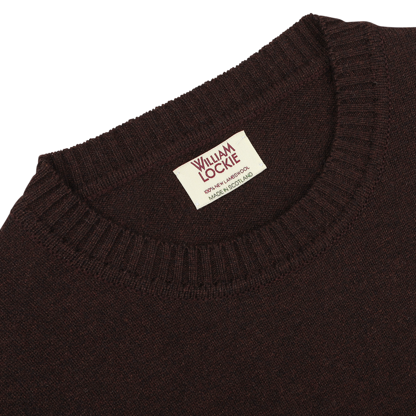 Close-up of an ebony brown William Lockie lambswool sweater featuring a visible tag that reads "William Lockie, Perthshire, Scotland, Made in Scotland." The sweater boasts a ribbed neckline.