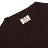 Close-up of an ebony brown William Lockie lambswool sweater featuring a visible tag that reads "William Lockie, Perthshire, Scotland, Made in Scotland." The sweater boasts a ribbed neckline.