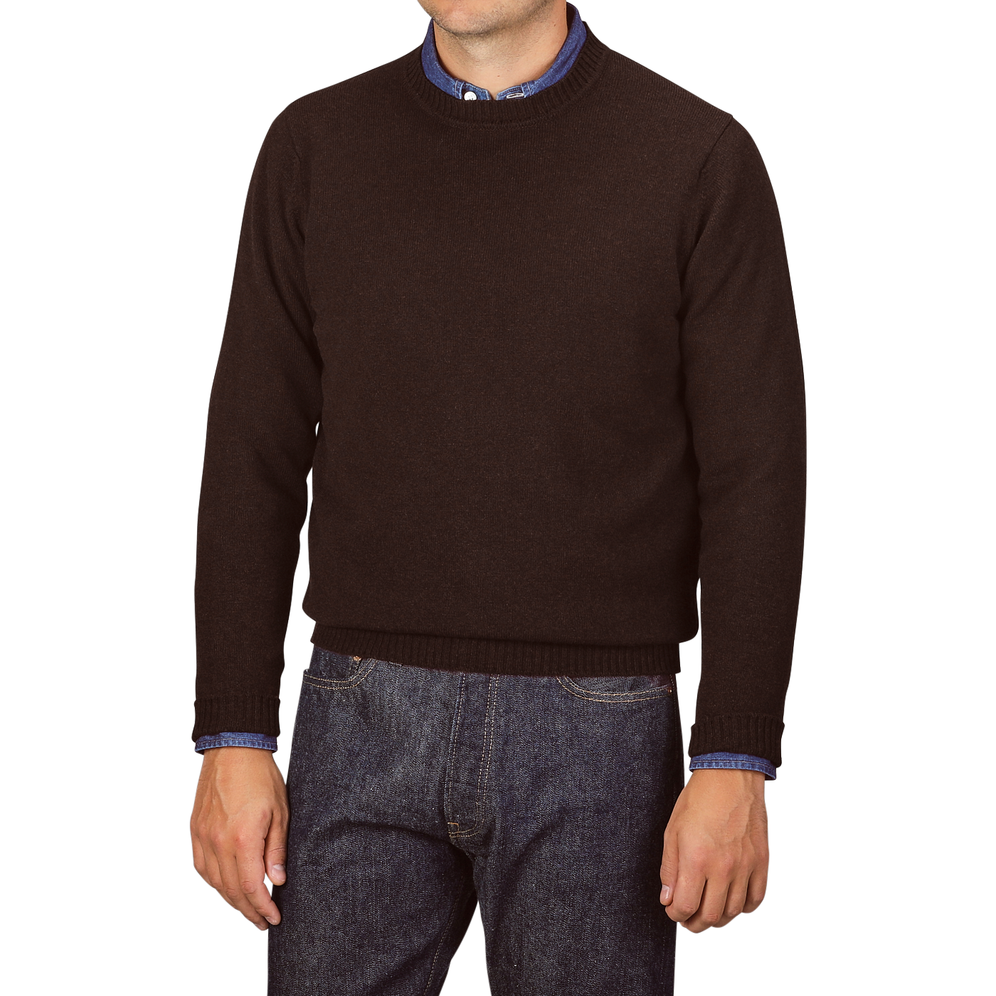 A person wearing a William Lockie Ebony Brown Crew-Neck Lambswool Sweater over a blue shirt with jeans, standing against a plain background.