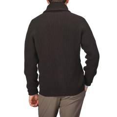 A person wearing a William Lockie Ebony Brown Lambswool Shawl Collar Cardigan and gray pants, viewed from behind, stands against a neutral background, their outfit subtly complemented by the soft texture of Scottish lambswool.