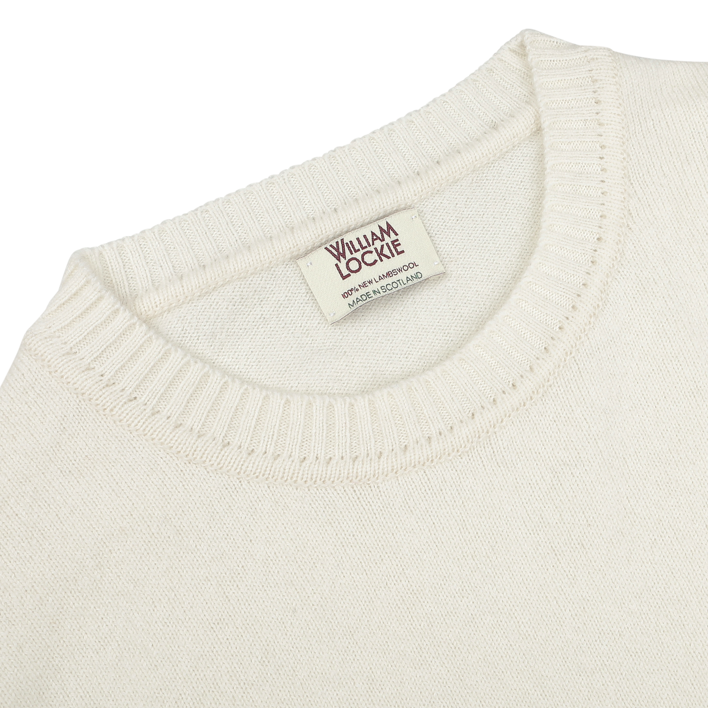 Close-up photo of an ecru crew neck lambswool sweater, with a label reading "William Lockie, Made in Scotland.