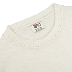 Close-up photo of an ecru crew neck lambswool sweater, with a label reading "William Lockie, Made in Scotland.