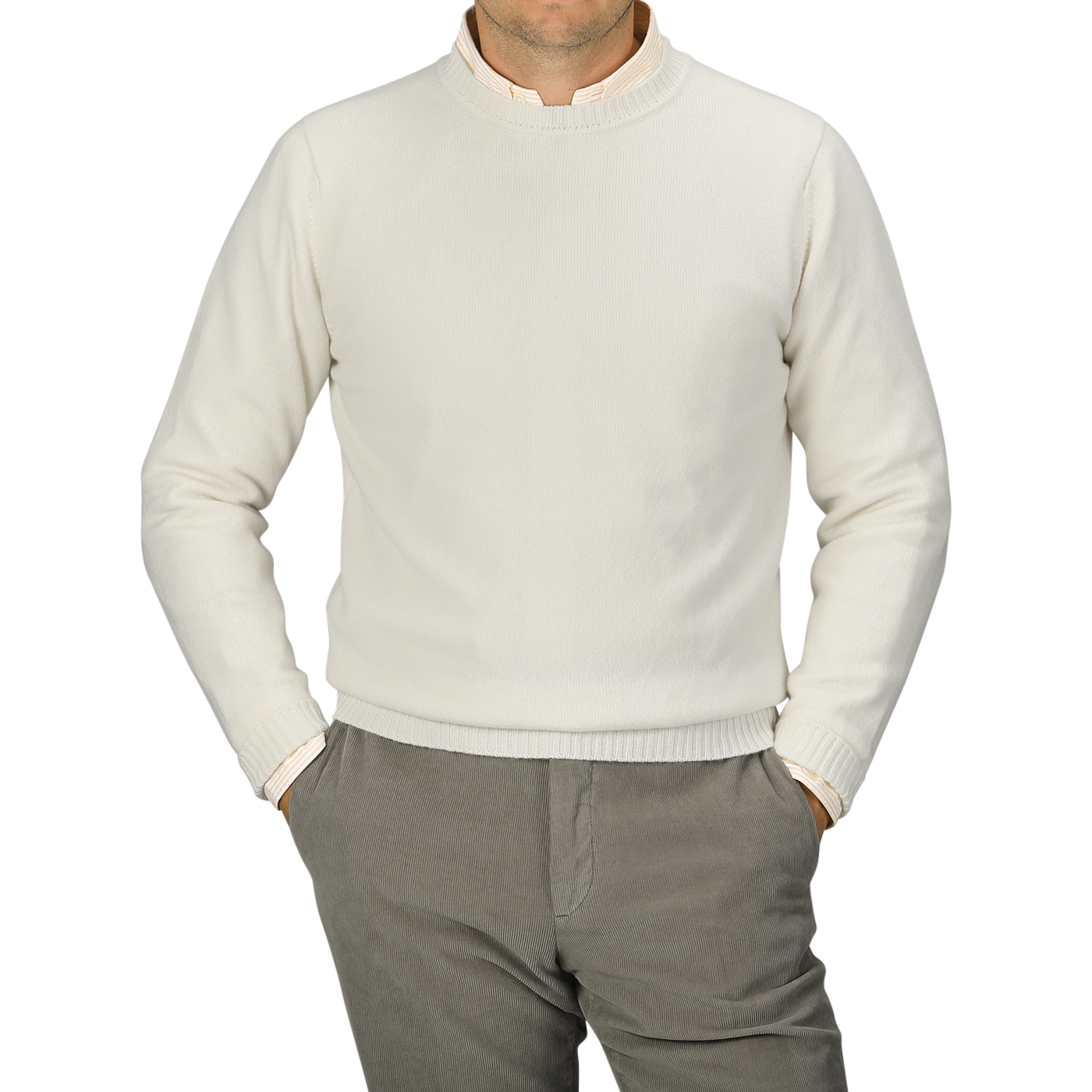 A person is wearing an Ecru Crew Neck Lambswool Sweater from William Lockie and light gray pants, standing with hands in pockets. The person's head is not visible. The background is plain gray, showcasing the elegance of quality knitwear.