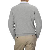 Image of a person seen from the back, wearing a William Lockie Flannel Grey Deep V-Neck Lambswool Sweater and beige pants. The person's left hand is in their pocket.