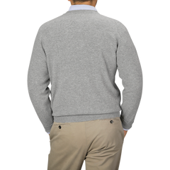 Image of a person seen from the back, wearing a William Lockie Flannel Grey Deep V-Neck Lambswool Sweater and beige pants. The person's left hand is in their pocket.