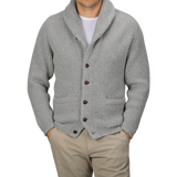 A person wearing a Flannel Grey Lambswool Shawl Collar Cardigan by William Lockie over a plain white t-shirt and beige pants, with hands in their pockets.