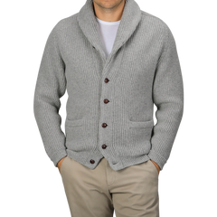 A person wearing a Flannel Grey Lambswool Shawl Collar Cardigan by William Lockie over a plain white t-shirt and beige pants, with hands in their pockets.