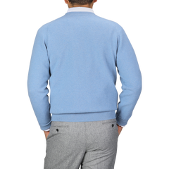 A person wearing a William Lockie Iceberg Blue Deep V-Neck Lambswool Sweater and gray pants is facing away from the camera against a plain background.