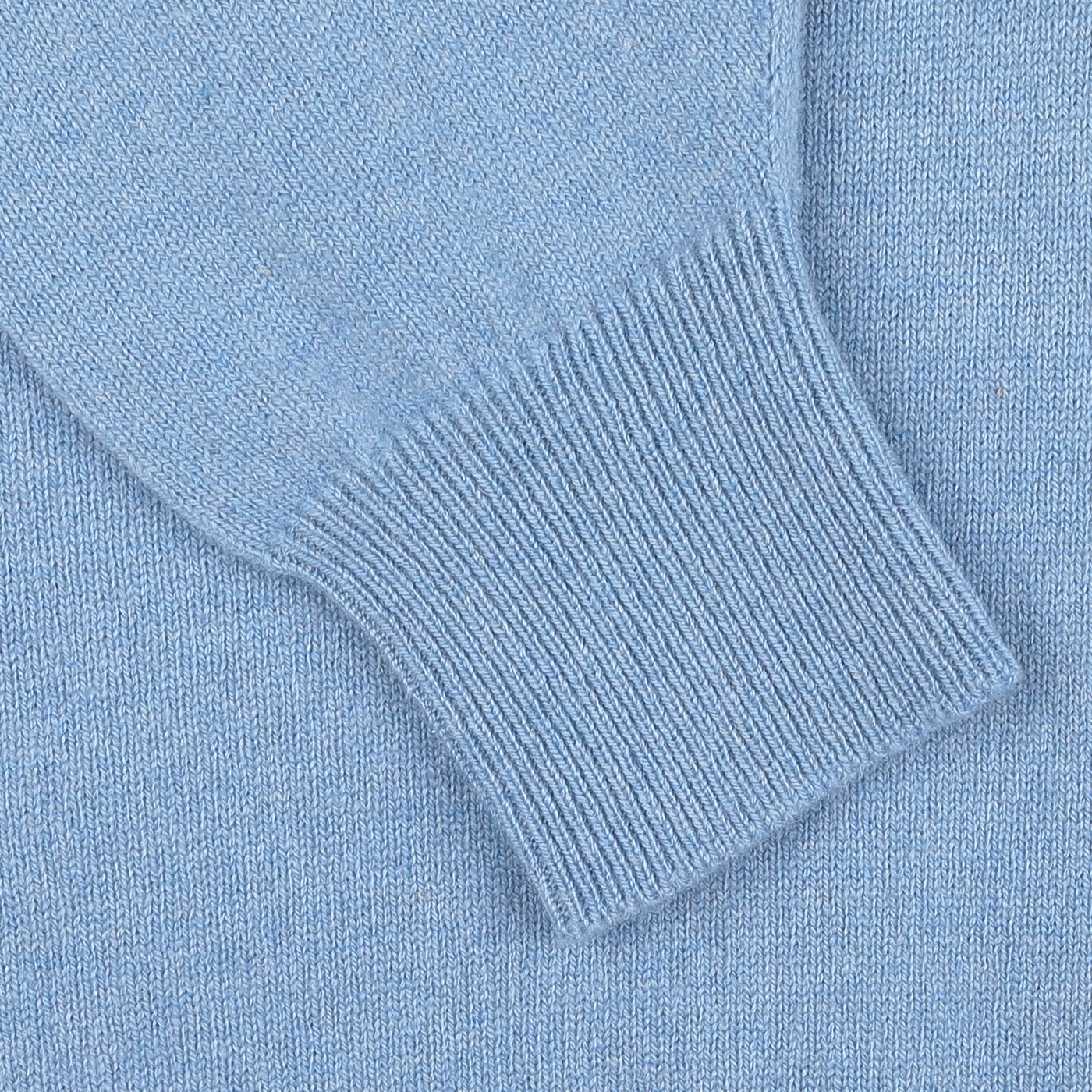 Close-up of a light blue knitted sweater sleeve with a ribbed cuff detail, part of the iceberg blue, regular fit deep V-neck lambswool sweater by William Lockie.