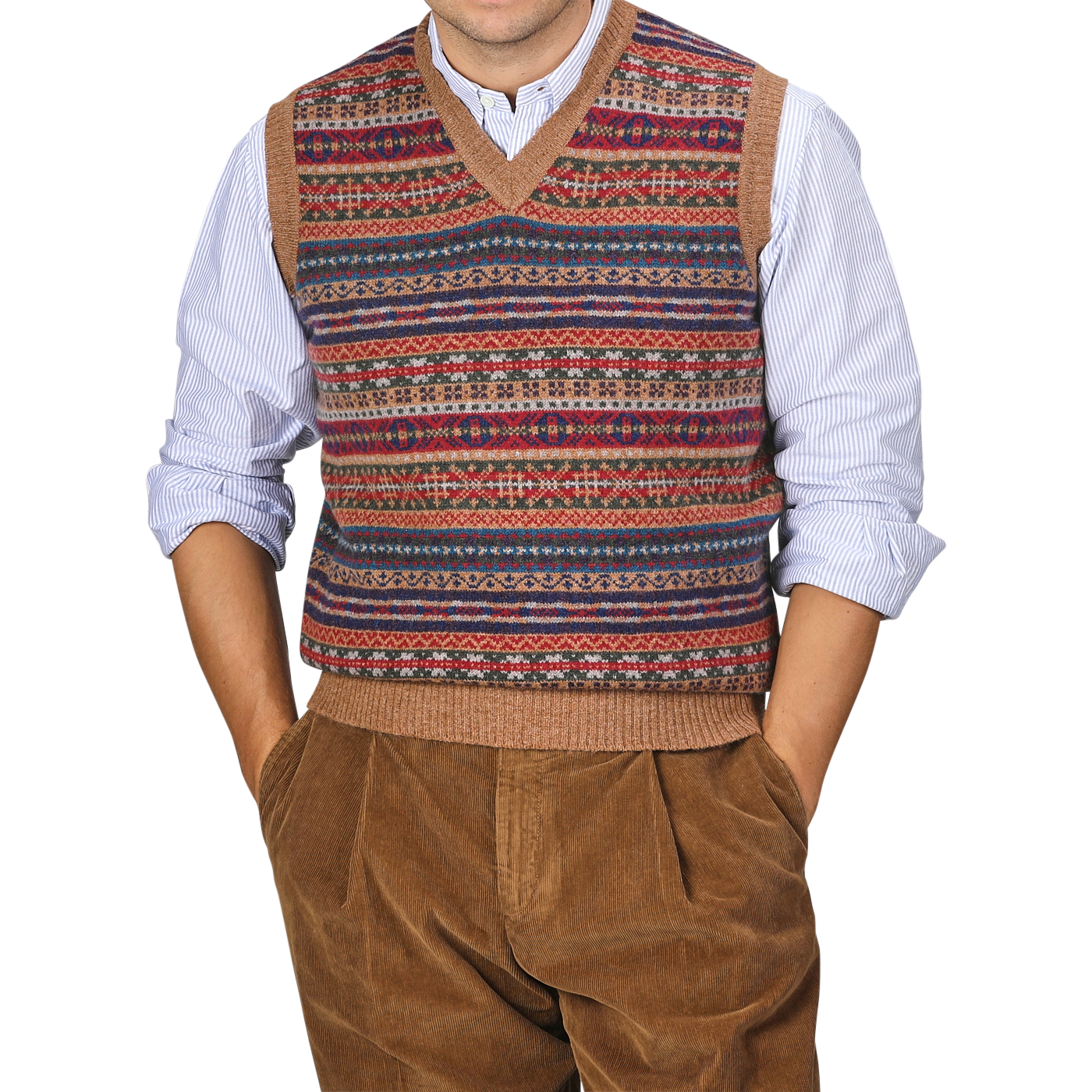 A person wearing a William Lockie Light Brown Fair Isle V-Neck Lambswool Slipover over a blue and white striped shirt, with hands in the pockets of brown corduroy pants.