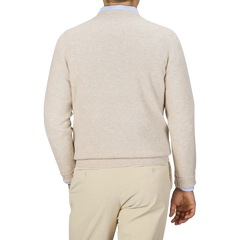 A person wearing a William Lockie Linen Beige Crew Neck Lambswool Sweater and khaki pants, viewed from the back, standing against a plain, neutral background. The outfit exudes timeless elegance, reminiscent of William Lockie's fine Scottish lambswool craftsmanship.