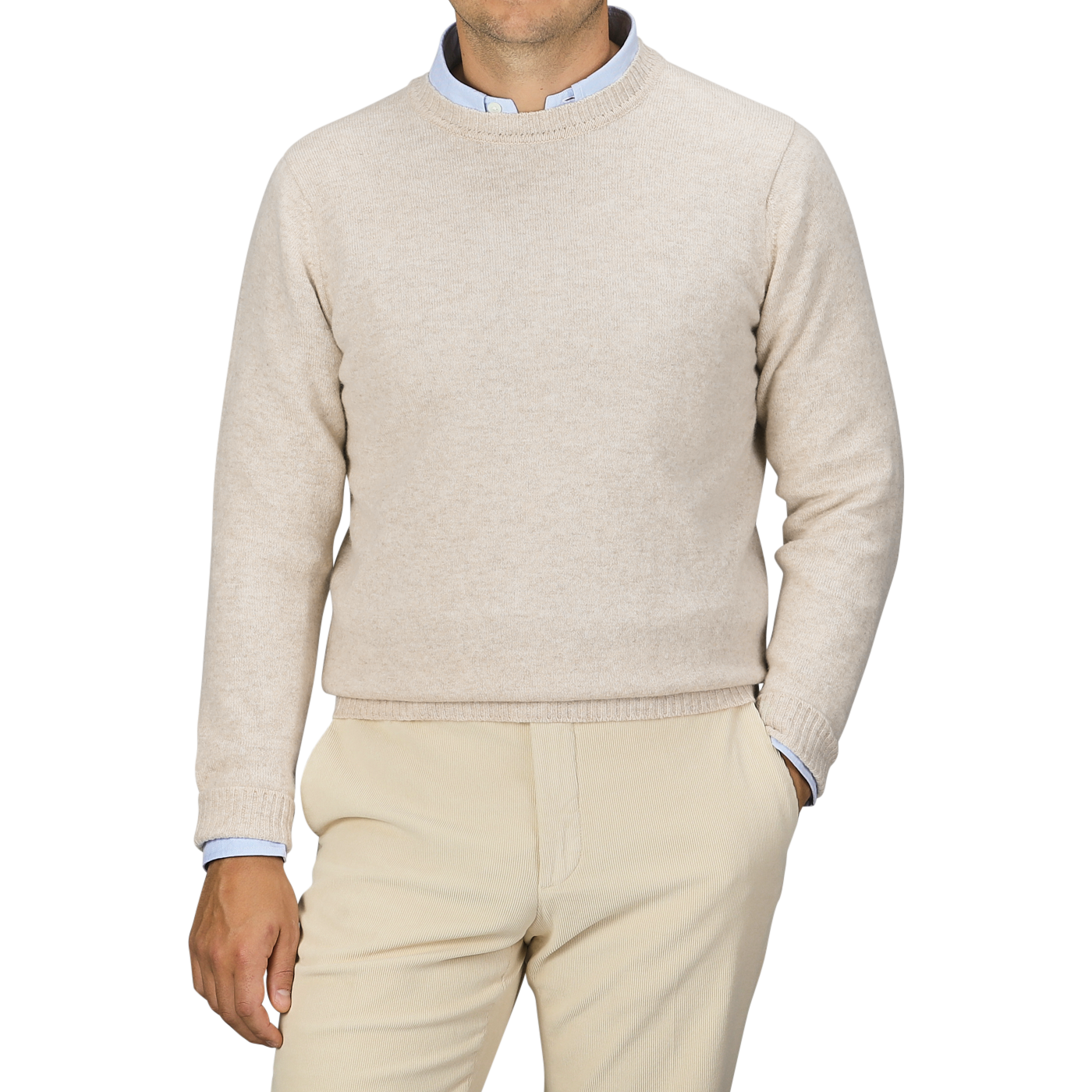 A person is wearing a William Lockie Linen Beige Crew Neck Lambswool Sweater over a light blue collared shirt, with matching beige pants, standing against a plain grey background.