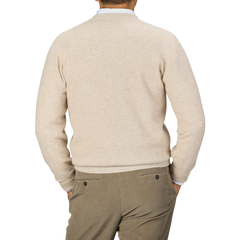 A person is shown from the back, wearing a Linen Beige Deep V-Neck Lambswool Sweater by William Lockie and light brown pants. Their hands are in their pockets.