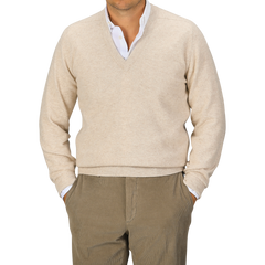 A person is wearing a William Lockie Linen Beige Deep V-Neck Lambswool Sweater over a white collared shirt, paired with light brown trousers. The person's head is partially out of the frame.