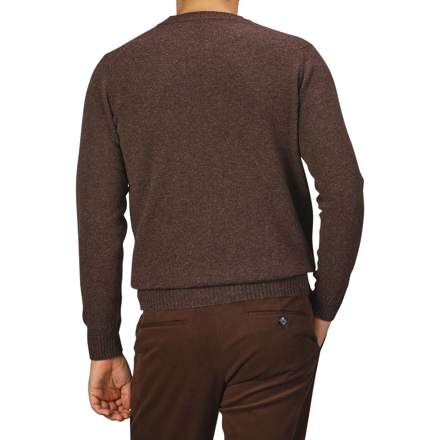 A person seen from the back wearing a mocha brown Mocha Brown Crew Neck Lambswool Sweater by William Lockie and brown pants, standing against a plain gray background. The knitwear fashion highlights the rich texture of the Scottish lambswool fabric.