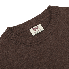 A close-up of the Mocha Brown Crew Neck Lambswool Sweater, crafted by William Lockie, showcasing its luxurious Scottish lambswool and the visible brand tag sewn onto the neckline.