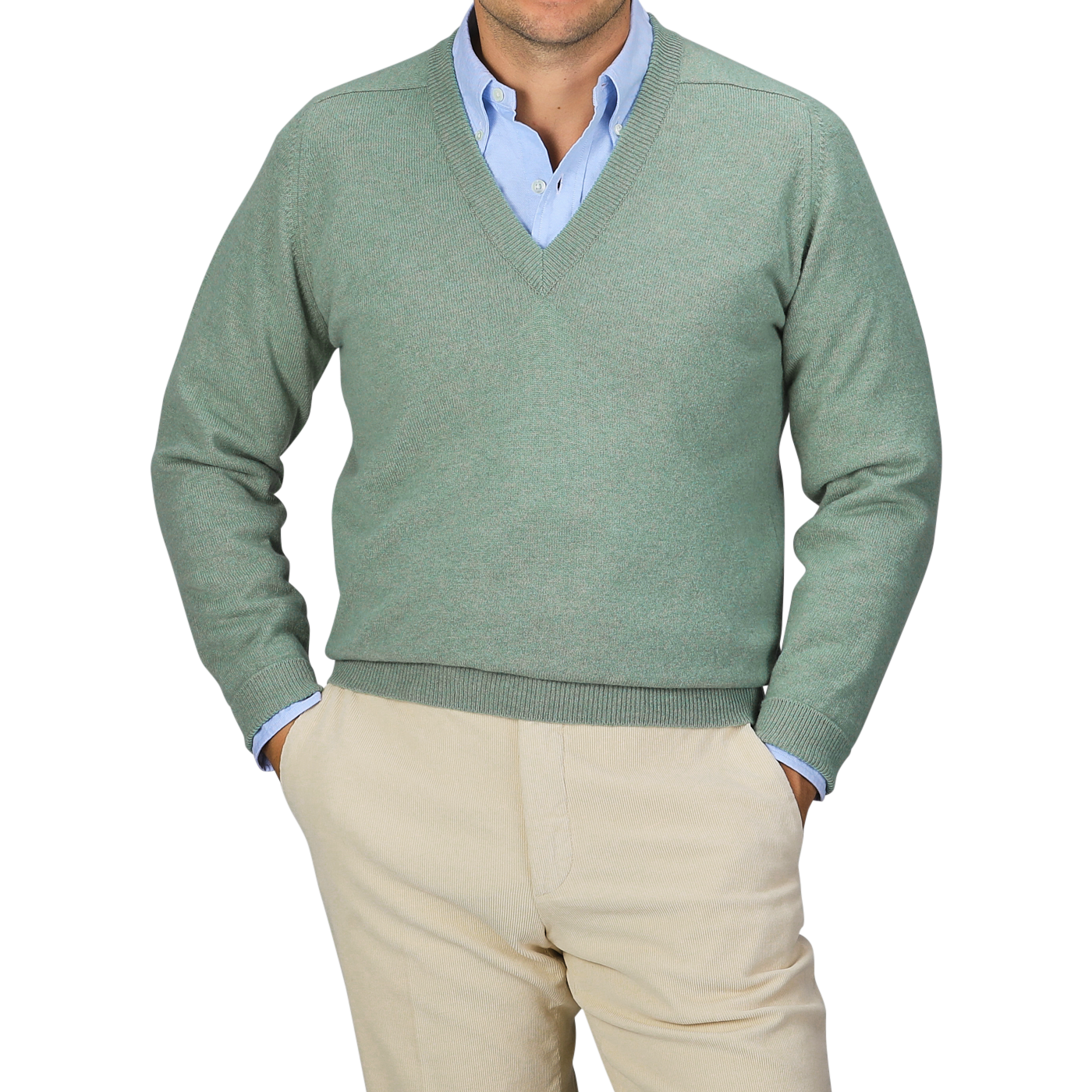 A person in a Mojito Green Deep V-Neck Lambswool Sweater by William Lockie over a blue collared shirt with beige pants, standing with hands in pockets against a gray background.