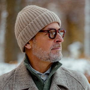 A man wearing glasses and a William Lockie Moondust Beige Cashmere Ribbed Beanie.