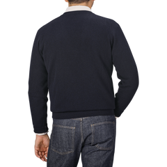 A man wearing a Navy Blue Deep V-Neck Lambswool Sweater by William Lockie and denim jeans is shown from the back against a plain gray background.