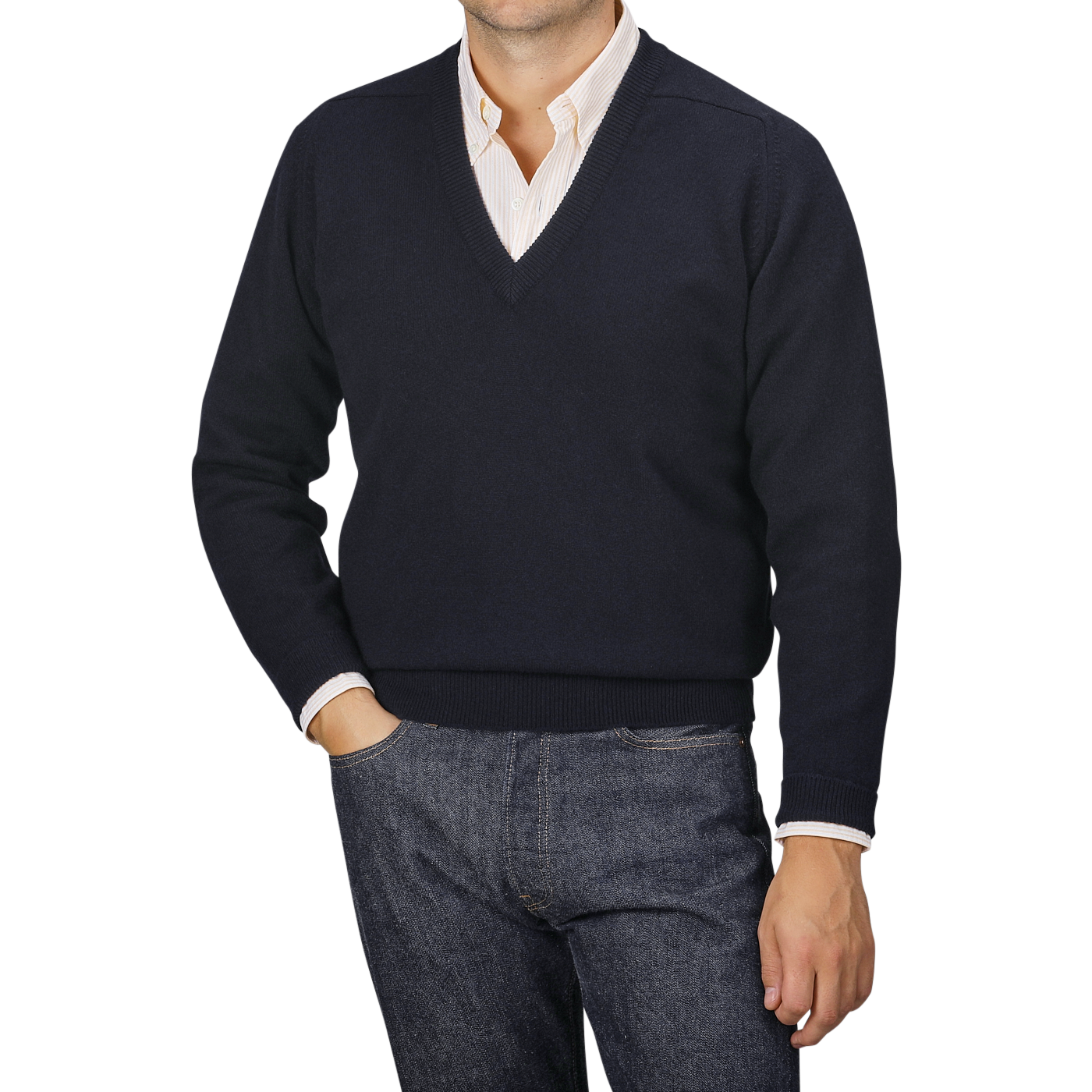 A person dressed in a navy blue deep V-neck lambswool sweater by William Lockie over a collared shirt and jeans, standing with one hand in their pocket against a neutral background.