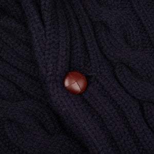 A close up of a William Lockie Navy Cable-Knit Lambswool Shawl Collar Cardigan with a red button.