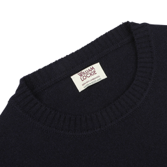 Close-up of a navy crew-neck lambswool sweater from William Lockie, with the label showing "WILLIAM LOCKIE Made in Scotland" sewn into the collar—perfect for smart casual occasions.