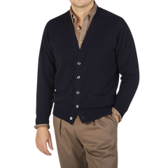 A man wearing a William Lockie Navy Lambswool Saddle Shoulder Cardigan sweater and tan pants made from Scottish lambswool.