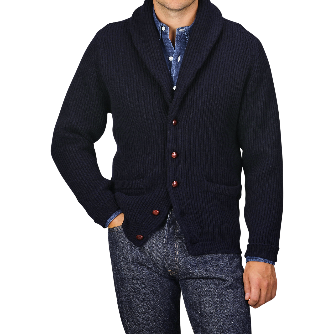 A person wearing a William Lockie Navy Lambswool Shawl Collar Cardigan over a blue button-down shirt and blue jeans, with their left hand in their pocket.