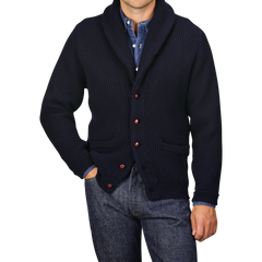 A person wearing a William Lockie Navy Lambswool Shawl Collar Cardigan over a blue button-down shirt and blue jeans, with their left hand in their pocket.