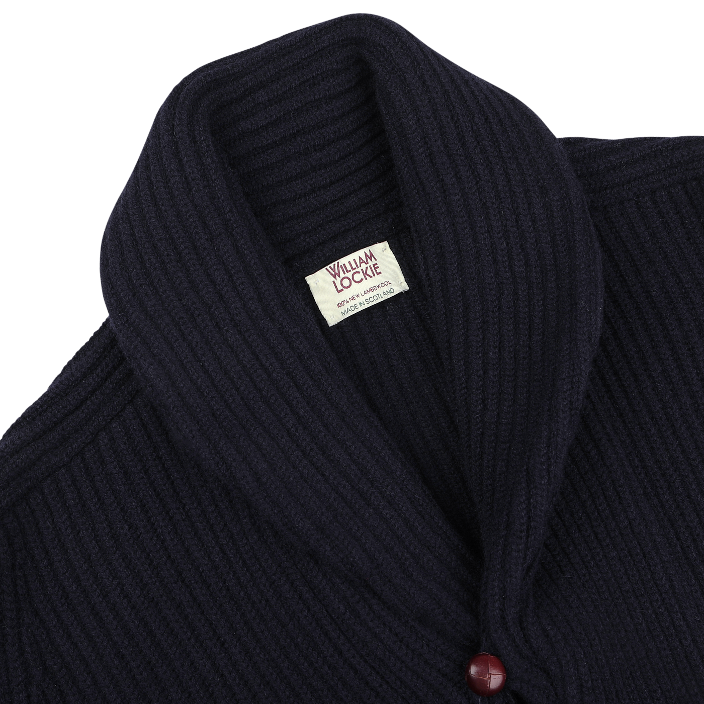 Close-up of the William Lockie Navy Lambswool Shawl Collar Cardigan, showcasing its dark blue ribbed design and luxurious Scottish lambswool fabric. The cardigan features distinctive leather buttons, with one red button visible near the bottom.