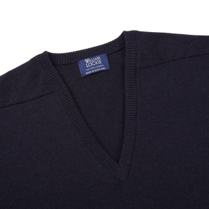 The William Lockie navy v-neck cashmere sweater, made from luxurious Scottish cashmere, is shown on a white background with its ribbed hems prominently displayed.