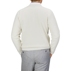 A person is wearing a William Lockie Off-White Deep V-Neck Lambswool Sweater and gray pants, standing with their back facing the camera against a plain background.