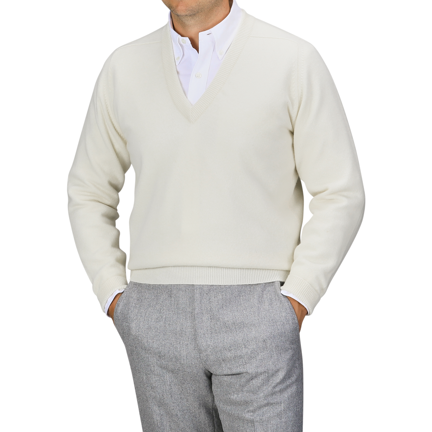 A person is wearing an off-white William Lockie Off-White Deep V-Neck Lambswool Sweater over a white collared shirt and gray trousers. The pose is casual with hands in their pockets.